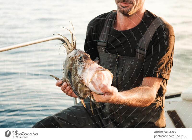 Crop man sitting on boat deck and holding fish with big mouth in daylight float marine water transport sail summer nature male ocean fishing tropical aqua