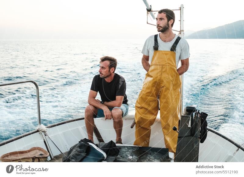 Young ethnic fishermen riding on fishing boat on rippling seawater fisherman travel sailboat mountain sky seascape ripple nature male young hispanic trip vessel