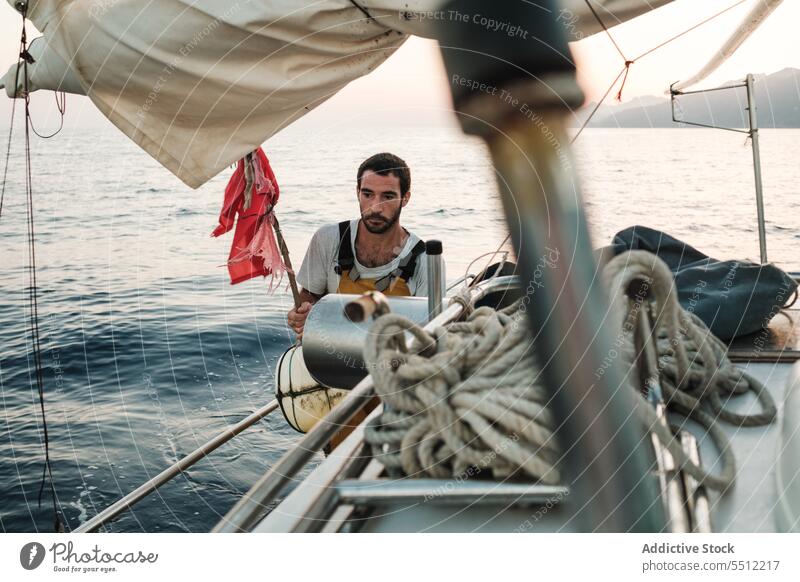 Focused young ethnic man standing with flag and buoy on sailboat in daylight lifesaver seascape travel trip nature summer male hispanic alone daytime wave