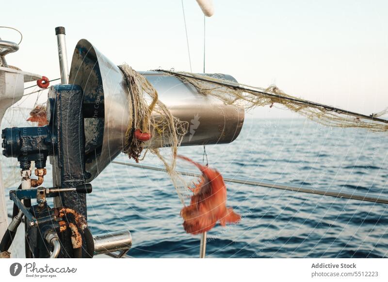 Fishing net on round drum of boat on rippling seawater with hanging red shrimp fishing marine nature ripple rope tied waterfront vessel daylight float catch