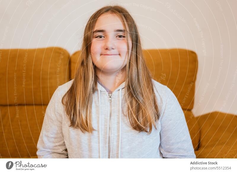 Smiling young girl in hoodie sitting on chair in living room smile positive sofa portrait appearance happy glad pleasant at home teen teenage style charming