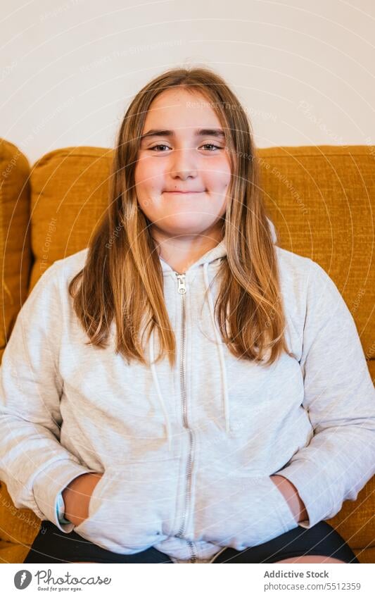 Smiling young girl in hoodie sitting on chair in living room smile positive sofa portrait appearance happy glad pleasant at home teen teenage cheerful style