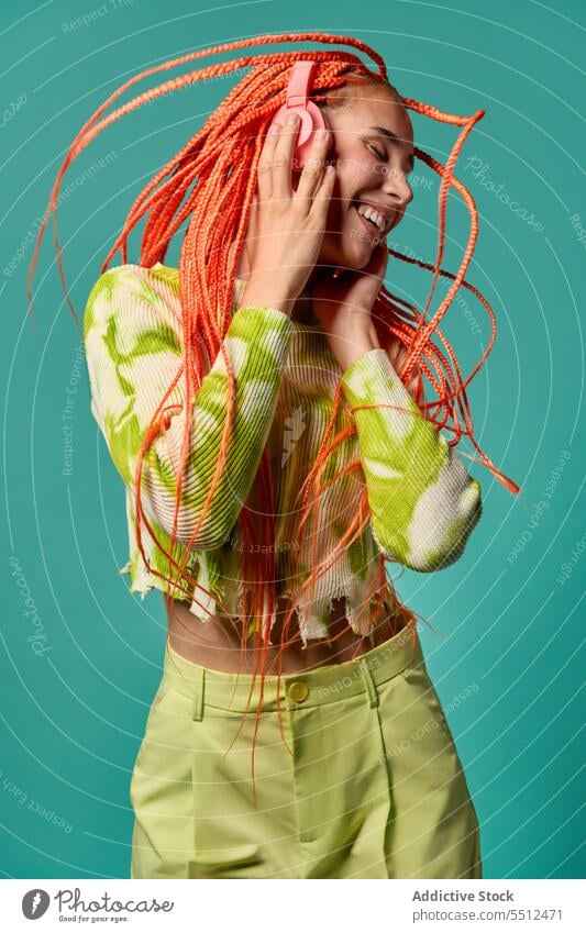 Cheerful woman with Afro braids listening to music on headphones dance vibrant portrait meloman stylish studio shot energy excited happy enjoy smile cheerful