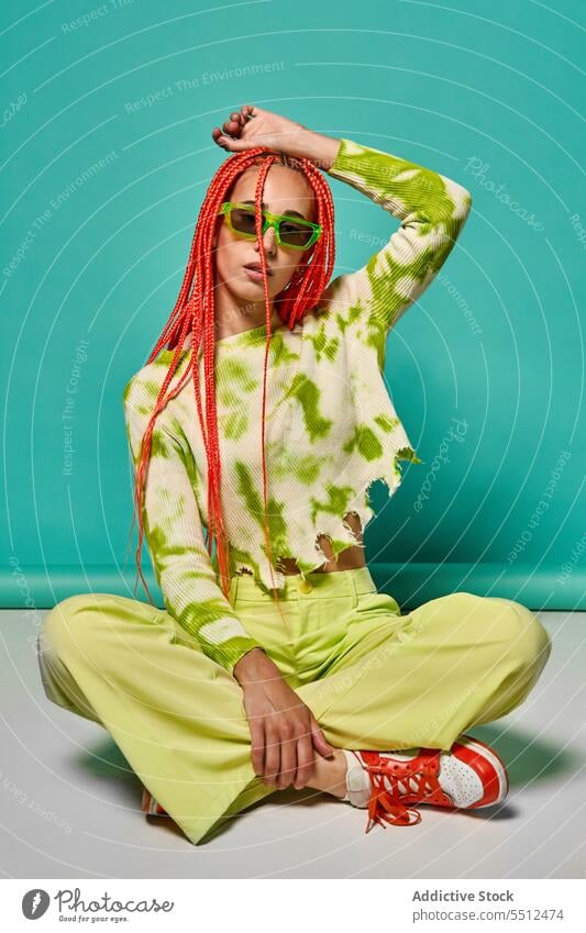 Trendy woman in stylish outfit sitting with legs crossed confident fashion hand on head model studio shot cool vivid unemotional young female afro braids