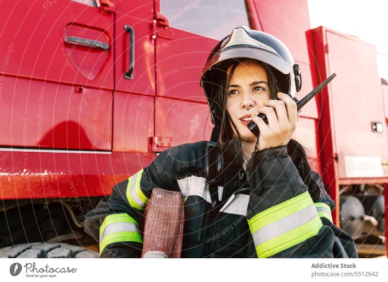 Female firefighter talking on radio near fire truck woman walkie talkie communicate hose emergency service job young female firewoman black hair safety