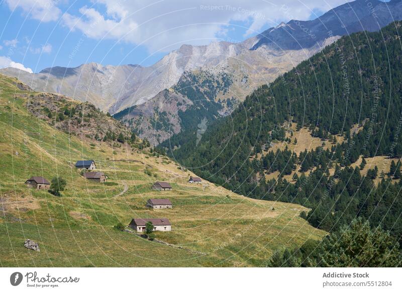 Settlement village on grassy green hill against mountain terrain under blue sky picturesque pyrenees range landscape nature highland houses Bachimala settlement