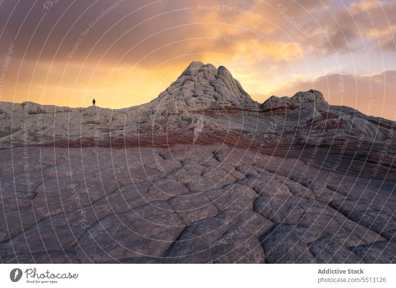 Anonymous traveler standing on stone during sunset mountain terrain boulder sky cloudy silhouette explore nature landscape adventure scenic rock journey tourism