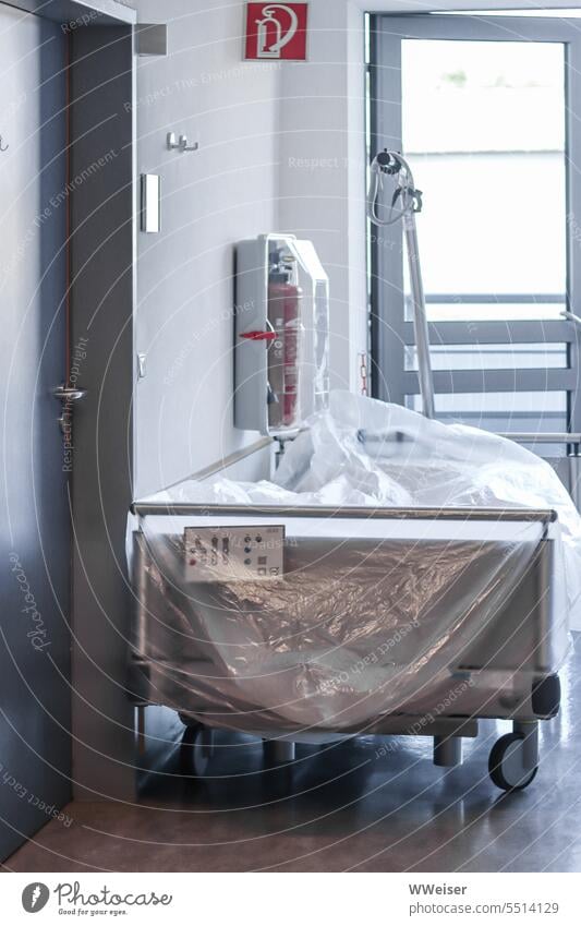 An unused hospital bed covered with a foil on the drafty corridor of a clinic Hospital Healthy Sick Illness Couch Bed Station Patient Unused Empty Wait