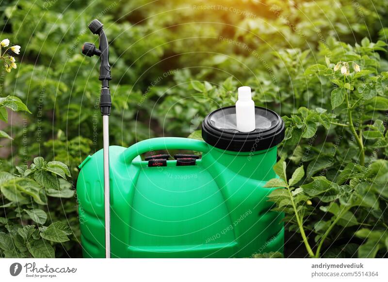 White little bottle of pesticide, herbicide for protecting plants from diseases and pests with mock up stands on container sprayer on natural green garden background. Agricultural seasonal work