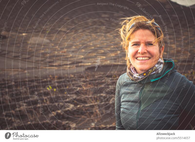 Portrait of smiling blonde middle aged woman in landscape with dark lava rocks Woman Middle aged woman Blonde blonde hair portrait pretty Adults naturally