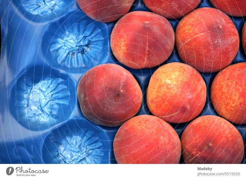 Fresh peaches in blue display and plastic packaging at a market and fruit stall in summer in the old town of Ayvalik on the Aegean Sea in Balikesir province, Turkey