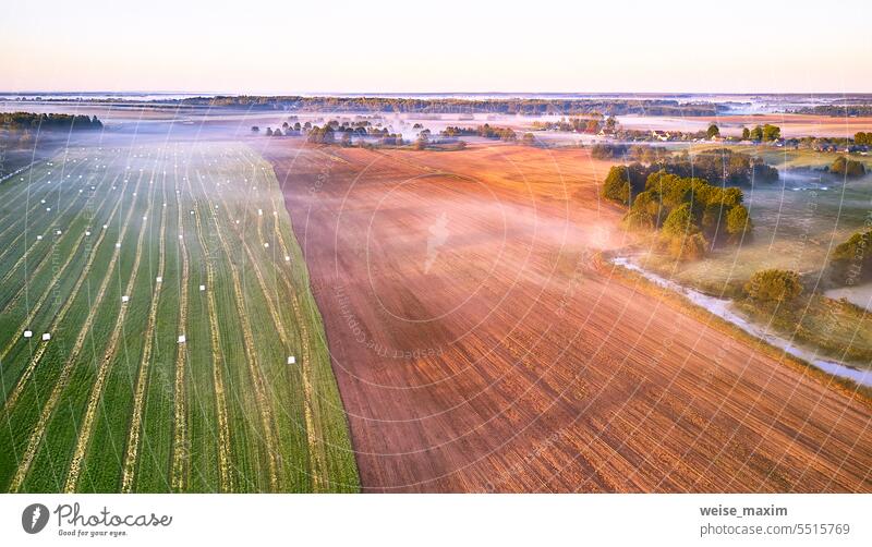 Warm sunny September morning. Autumn beautiful fog landscape. Small river curves in trees. Bright sunny misty riverside. Scenic view of rural sunrise. Village in Agriculture fields.