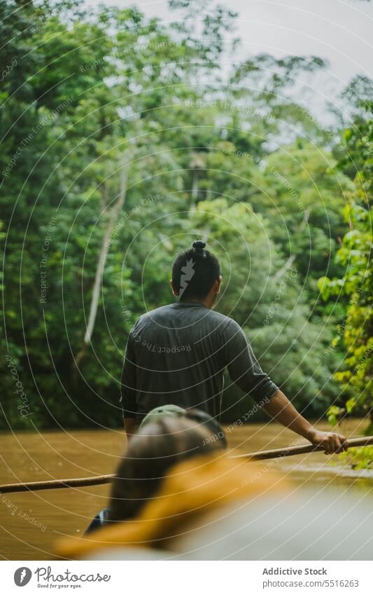 Anonymous ethnic man sailing on traditional boat local fisherman indigenous float tropical river huaorani jungle tribe village amazon rainforest oar authentic