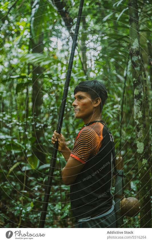 Tribal man with long stick in forest tropical nature bag environment serious exotic green male summer woods plant tree foliage natural flora season greenery