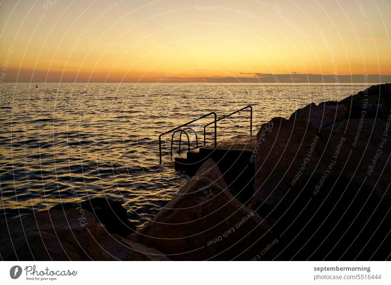 Sea in evening mood Ocean Stairs leading into the water Foreground stones Yellow tones and black Exterior shot Nature Evening Sunset Deserted