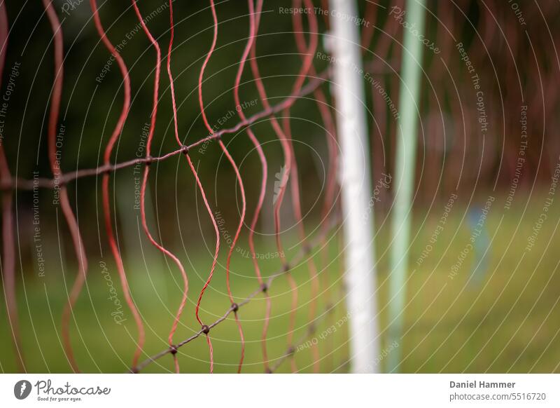 Orange sheep protection fence with white and green rod on a green meadow. In the background a blurred row of trees. Sheep net Sheep fence Electrified fence