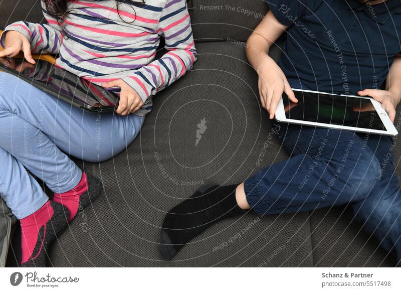 two children sitting side by side on the couch playing on their tablets gaming Ipad gambling Technology Playing Internet Computer Online Digital Education