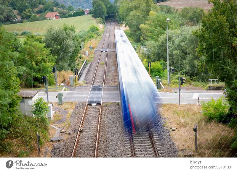 moving train crosses a road at a level crossing. Motion blur Passenger train Railroad crossing Railroad tracks Rail transport Public transit Railroad system