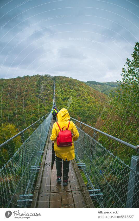 juneg woman in yellow raincoat walks across geierlay suspension bridge in bad weather Bad weather Rain Wet Raincoat Rain jacket Yellow Gray Suspension bridge