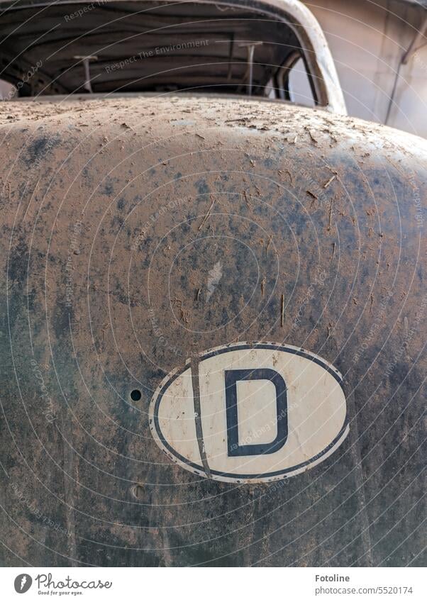 The frame of a classic car is completely filthy in a long abandoned Lost Place. On the tailgate is a sticker with a large D lost place Vintage car