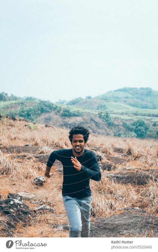 a young man running up a hill in a black shirt. Hill Nature Green Sky Meadow Blue Landscape Grass Exterior shot Environment Field Beautiful weather mountain