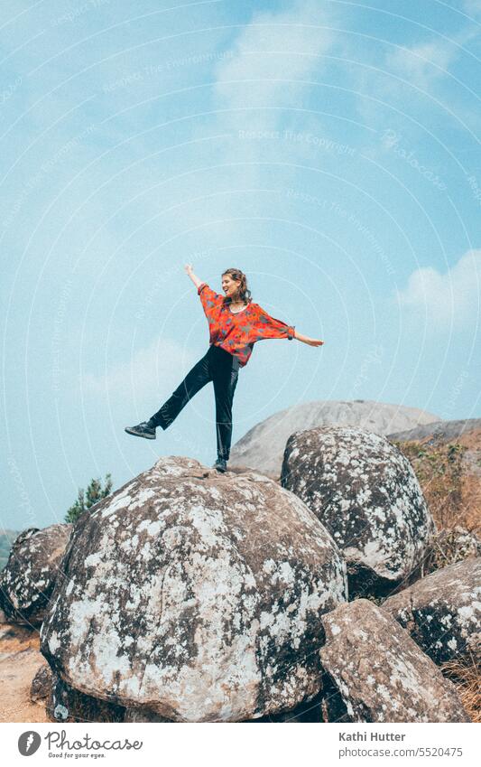 a young woman is standing on a big stone, behind it the blue sky is shining. She wears a red blouse and black pants. Sky Clouds Woman Blue Summer Sun