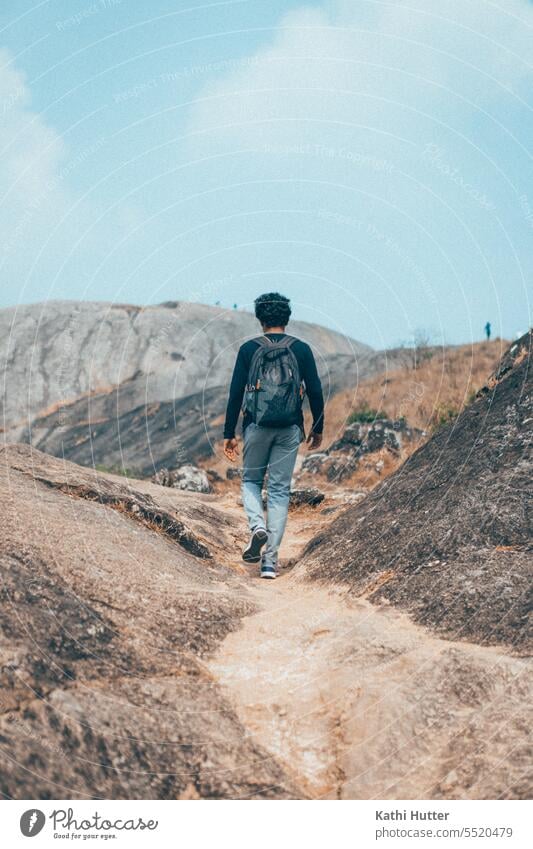 a young man with a backpack on his back walks in the mountains with rocky big stones Hiking Walking backpacker Backpack Mountain Tourism Vantage point Landscape