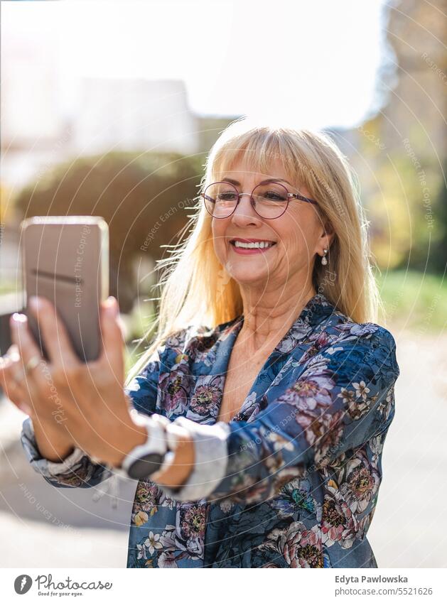 Portrait of smiling senior woman with mobile phone in the street natural enjoy satisfied cheerful confident pensioner outdoors outside eyeglasses elderly