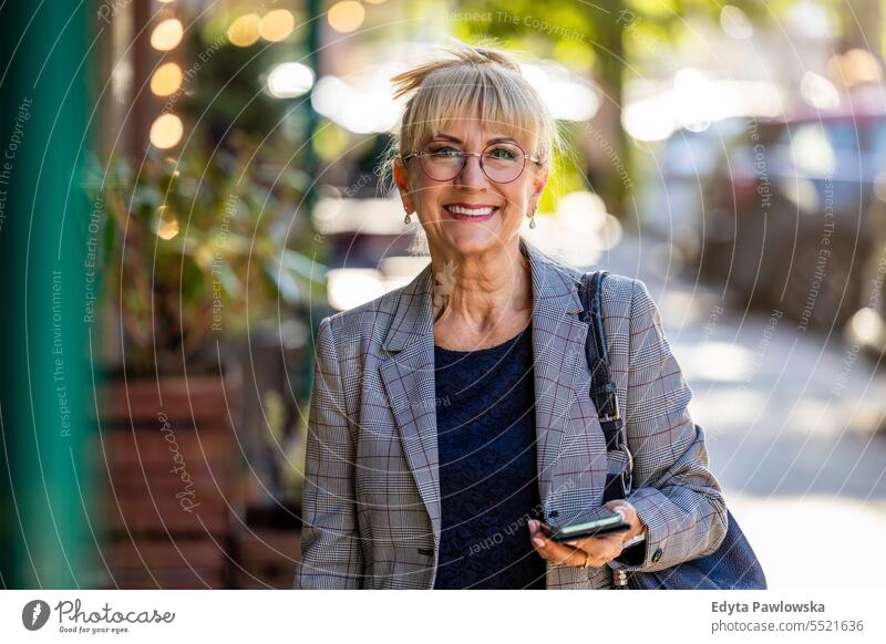 Portrait of smiling senior woman with mobile phone in the street natural enjoy satisfied cheerful confident pensioner outdoors outside eyeglasses elderly