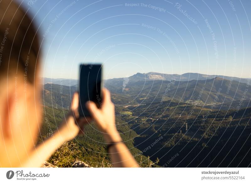 A happy young woman takes pictures of the landscape with her smartphone from the top of a mountain. nature travel mountains sky view outdoors beauty forest