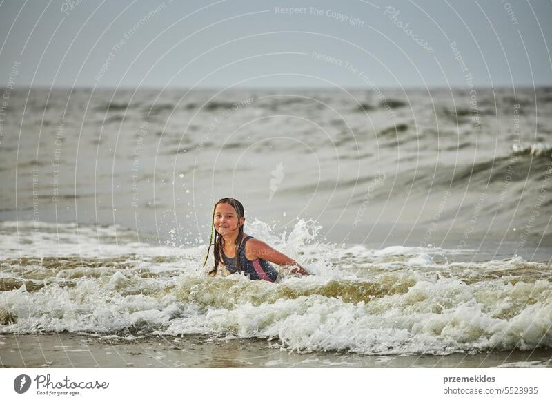 Little girl playing with waves in the sea. Kid playfully splashing in waves. Child jumping in sea. Vacations on the beach. Water splashes summer vacations ocean