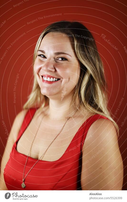 Portrait of blonde beautiful smiling woman in red dress in front of red wall Woman portrait Long-haired long hairs Face naturally pretty Authentic Attractive