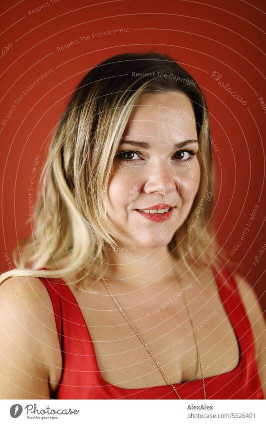 Portrait of blonde beautiful smiling woman in red dress in front of red wall Woman portrait Long-haired long hairs Face naturally pretty Authentic Attractive