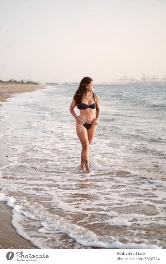 Carefree woman in bikini on beach bra sea vacation style attractive summer ocean female young slim coast charming nature dark hair lady stand water sensual