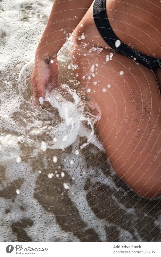 Crop woman splashing seawater on seashore at beach bikini motion foam vacation summer wave coast ocean wet swimwear trip travel tourism recreation lady seaside