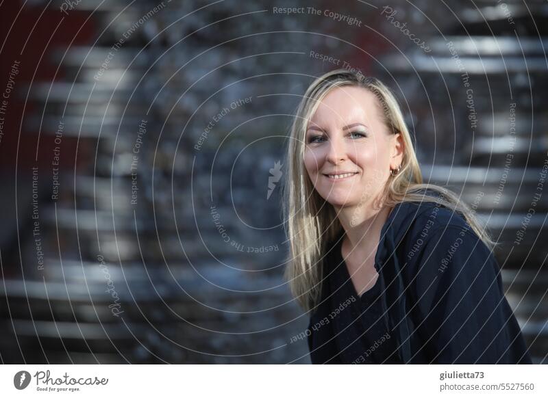 Happy woman with long blond hair sits smiling in afternoon sun in front of fountain portrait Woman Feminine Adults Exterior shot Shallow depth of field