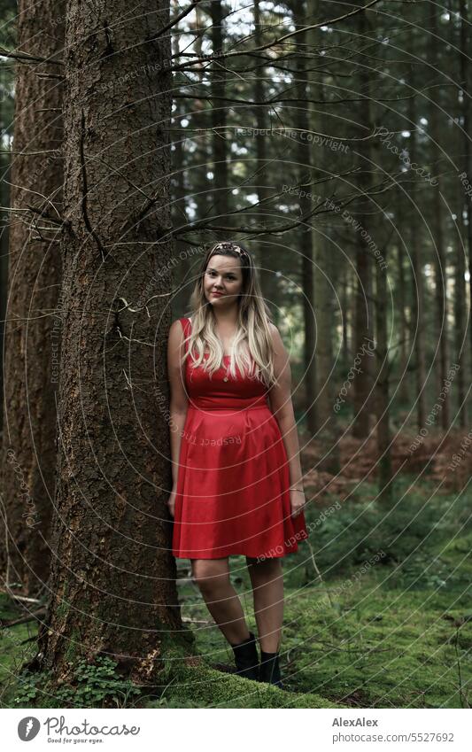 Portrait of beautiful blonde long haired woman standing in a light forest leaning against a tree and looking at the camera Woman pretty Blonde Long-haired