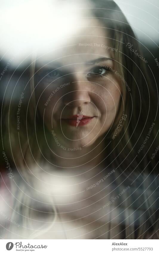 Blonde woman looking through window pane with reflections directly into camera Woman portrait Long-haired long hairs Reflection Face naturally pretty Authentic