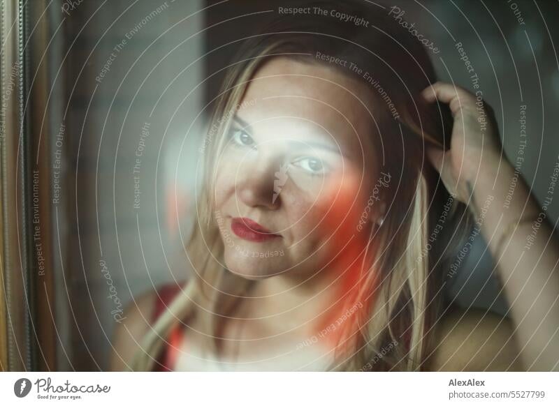 Blonde woman looks through a window pane with reflections directly into the camera - in the pane is the reflection of a life ring Woman portrait Long-haired