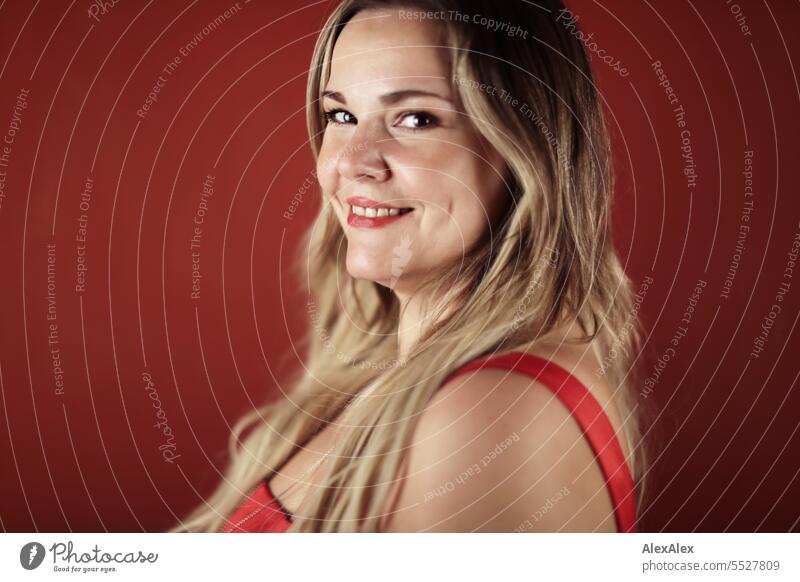 Portrait of blonde beautiful smiling woman in red dress in front of red wall Woman portrait Long-haired long hairs Face naturally pretty Authentic Attractive