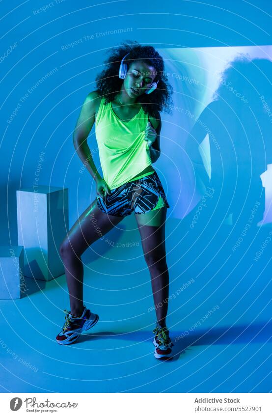 Black woman in headphones standing hand on waist studio shot sport listen music fitness audio melody female sportswoman meloman sound activewear wellness