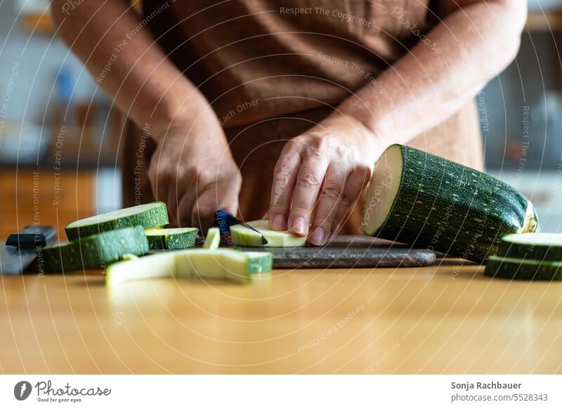 A woman cuts a zucchini on a wooden cutting board. Zucchini Chopping board Knives Woman hands Vegetable Cooking Kitchen Table Healthy Eating Close-up Food Diet