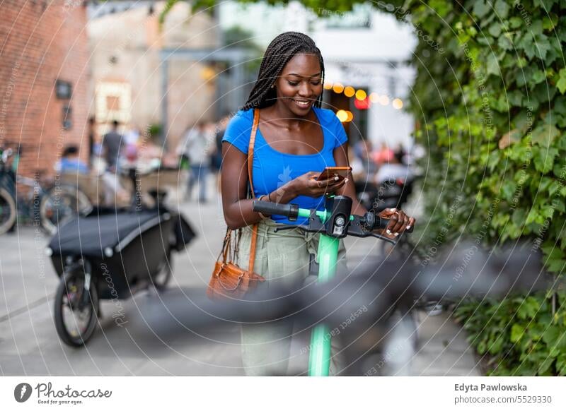 Portrait of happy young woman using her smartphone while standing with electric scooter in the city adult attractive beautiful black confidence confident cool