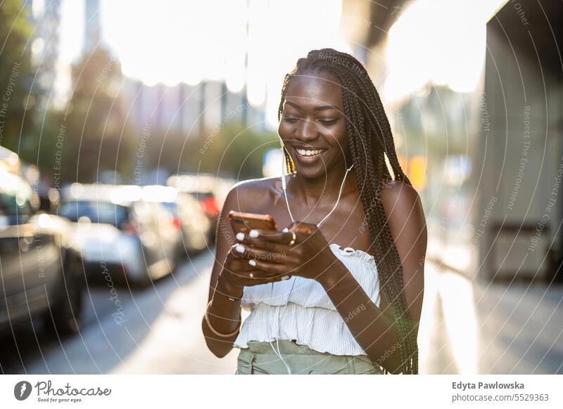 Young woman listening to music with earphones in the city adult attractive beautiful black confidence confident cool female girl hairstyle leisure lifestyle