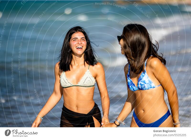 Two pretty young woman having fun on the seaside adult beach beautiful bikini carefree cheerful enjoy enjoyment female free time friends friendship happiness