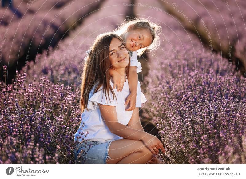 Happy family in purple lavender field. young beautiful mother and child Girl enjoy walking blooming meadow on summer day. Mom having fun with pretty daughter in nature on sunset. mothers day