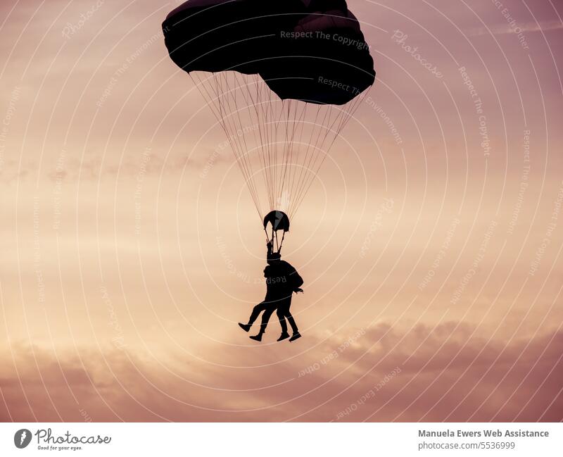 A tandem team glides through the evening sky by parachute. It looks like they are walking on clouds. hang out Skydiving Parachute parachute jumping Tandem