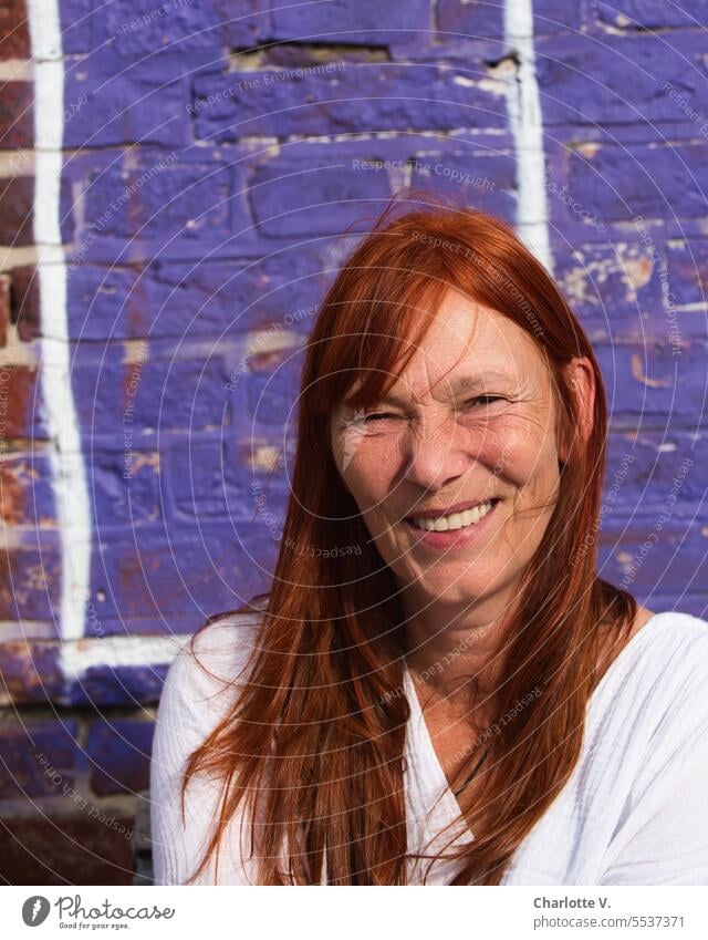 Wide land | Squinting against the sun | Smiling redhead woman in front of purple wall Human being person Woman 1 Person portrait portrait of a woman Red-haired