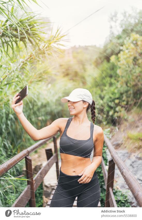 Female hiker taking selfie in forest woman smile break weekend travel smartphone female woods happy hat self portrait glad traveler tree nature mobile brunette