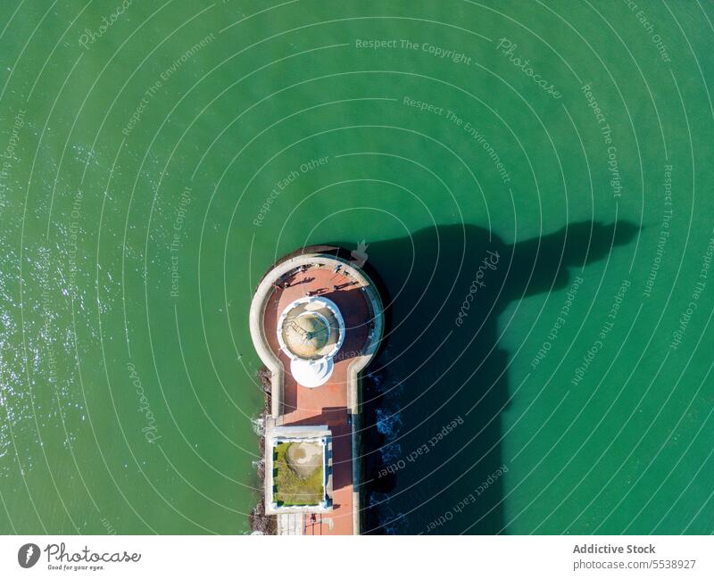 Drone view of lighthouse with shade on seacoast in daylight shore road beacon construction architecture seascape asphalt ocean seashore nature seafront water